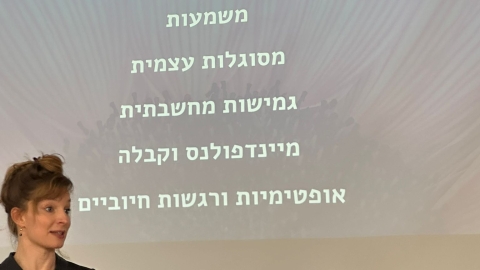 אישה שמאחוריה מופיעה שקופית של מקרן וכתוב בה גמישות נפשית מערכות יחסים משמעות מסוגלות עצמית גמישות מ
