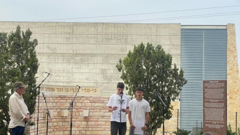 ילדים עומדים עם דפים ביד ואחד מהם מקריאה למיקרופון.jpg