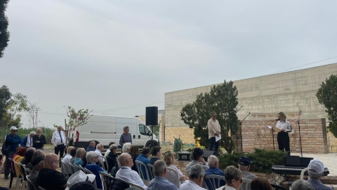 אישה עומדת מול אנשים ומחזיקה דף ומדברת למיקרופון.jpg