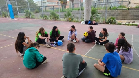 ילדים יושבים במעגל במגרש ומחזיקים כדור צהוב.jpg