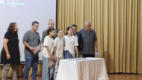 אנשים  עומדים על במה ליד שולחן חלוקת תעודות.jpg