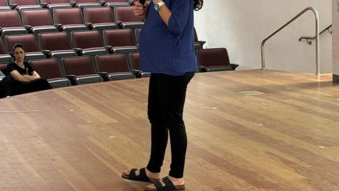 אישה עומדת על הבמה ומחזיקה מיקרופון.jpg