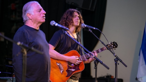 שני אנשים עומדים על במה ושרים אחד מהם גם מנגן בגיטרה.jpg