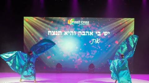 רקדניות על הבמה ומאחוריהן יש מסך כתוב יש בי אהבה והיא תנצח.jpg