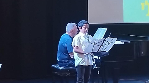 איש וילד מנגנים על במה. מאחוריהם מצגת שכתוב עליה קונצרט סיום השנה של מוסיקלי.jpg