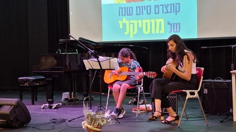 אישה וילדה מנגנות על במה. מאחוריהם מצגת שכתוב עליה קונצרט סיום השנה של מוסיקלי.jpg