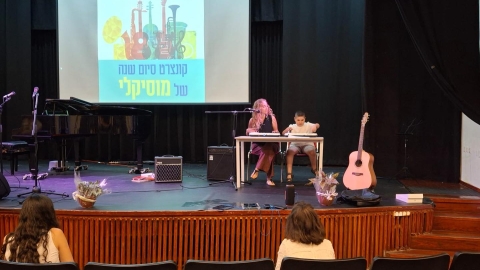 אישה וילד מנגנים על במה. מאחוריהם מצגת שכתוב עליה קונצרט סיום השנה של מוסיקלי.jpg