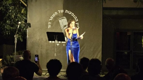 אישה בשמלה כחולה עומדת על הבמה ומחזיקה מיקרופון.jpg