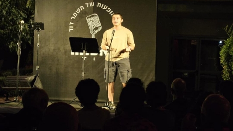 איש בחולצה לבנה עומד על הבמה ומחזיקה מיקרופון.jpg