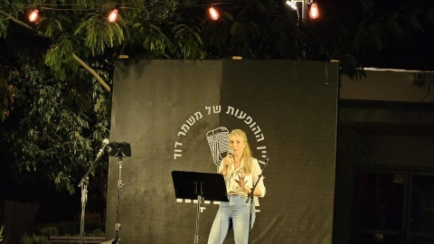 אישה בחולצה לבנה עומדת על הבמה ומחזיקה מיקרופון.jpg