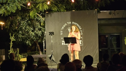 אישה בשמלה ורודה עומדת על הבמה ומחזיקה מיקרופון.jpg