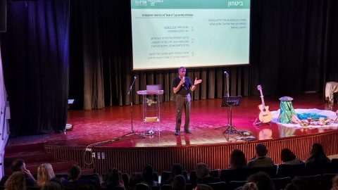 איש עומד על במה ומאחוריו שקף מצגת בנושא ביטחון.jpg