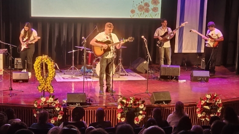 איש שר ומחזיק גיטרה. מאחוריו יש נגנים.jpg