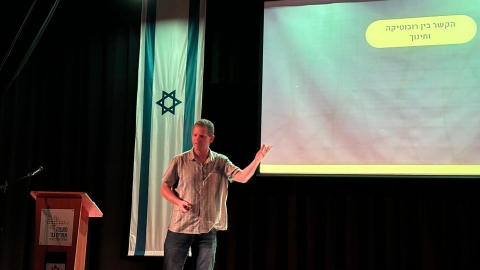 איש עומד  על הבמה ומאחוריו מצגת.jpg