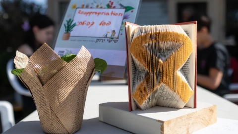 סמל החטופים עשוי מעמודים של ספר. לידו עציץ עטוף ביוטה.jpg