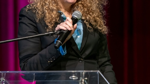 ישה עומדת על במה ומחזיקה מיקרופון.jpg