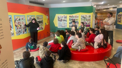 ילדים יושבים ומדריכה מסבירה להם על מייצגי הקומיקס.jpg