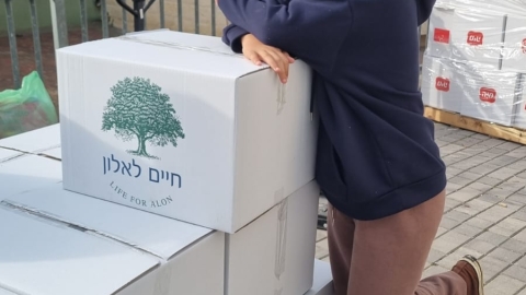 תלמידה מחייכת ונשענת על הארגזים עם משלוחי המנות שנארזו.jpeg