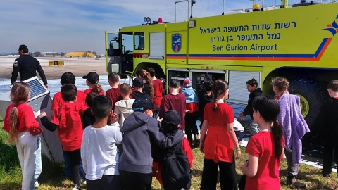 תלמידי בית ספר שחקים עומדים ליד רכב תפעול בשדה התעופה.jpeg