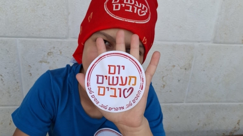 ילד מחזיק מדבקה שכתוב עליה יום המעשים הטובים.jpg