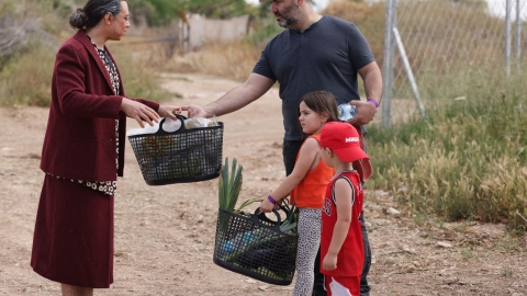 שחקן בדמות גברת עם סלים נותן את סלי הקניות שלו לצועדים.jpg