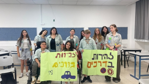 חניכים בתנועת נוער מחזיקים שלט עליוכתוב זהירות בדרכים.jpeg