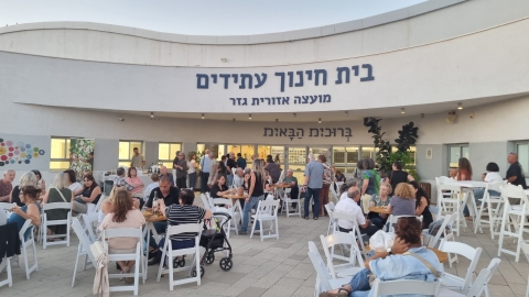 אנשים יושבים סביב שולחנות לבנים ברחבת בית החינוך עתידים.jpg