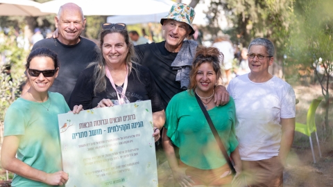 צוות הגינה הקהילתית של מושב סתריה עם שלט של הגינה.jpg